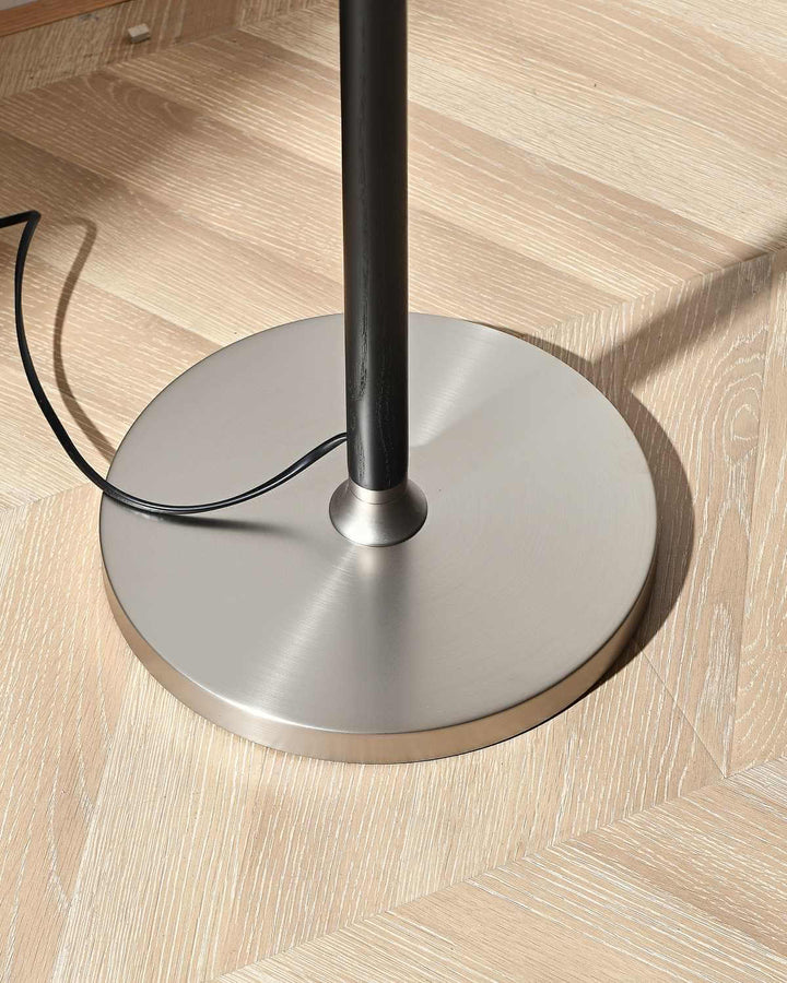 Base of a minimalist curved floor lamp showcasing a sleek metallic design on a wooden floor.