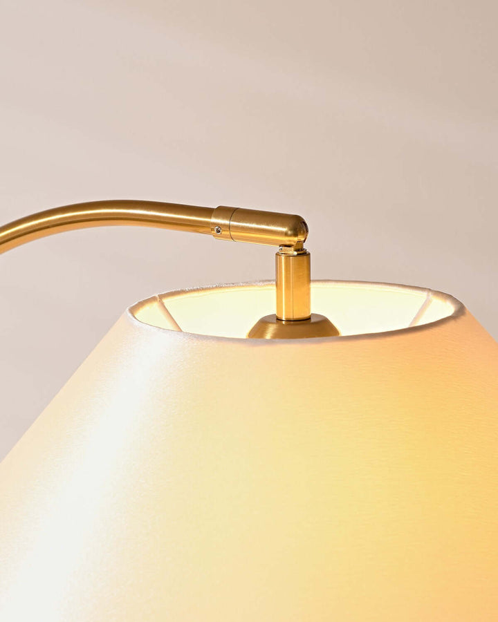 Close-up of Nelke curved floor lamp's elegant brass arm and soft fabric shade, perfect for minimalist decor.