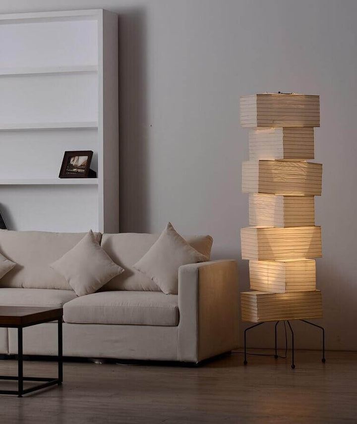 Warm Akari rice paper floor lamp beside a white sectional sofa in a softly lit minimalist living room