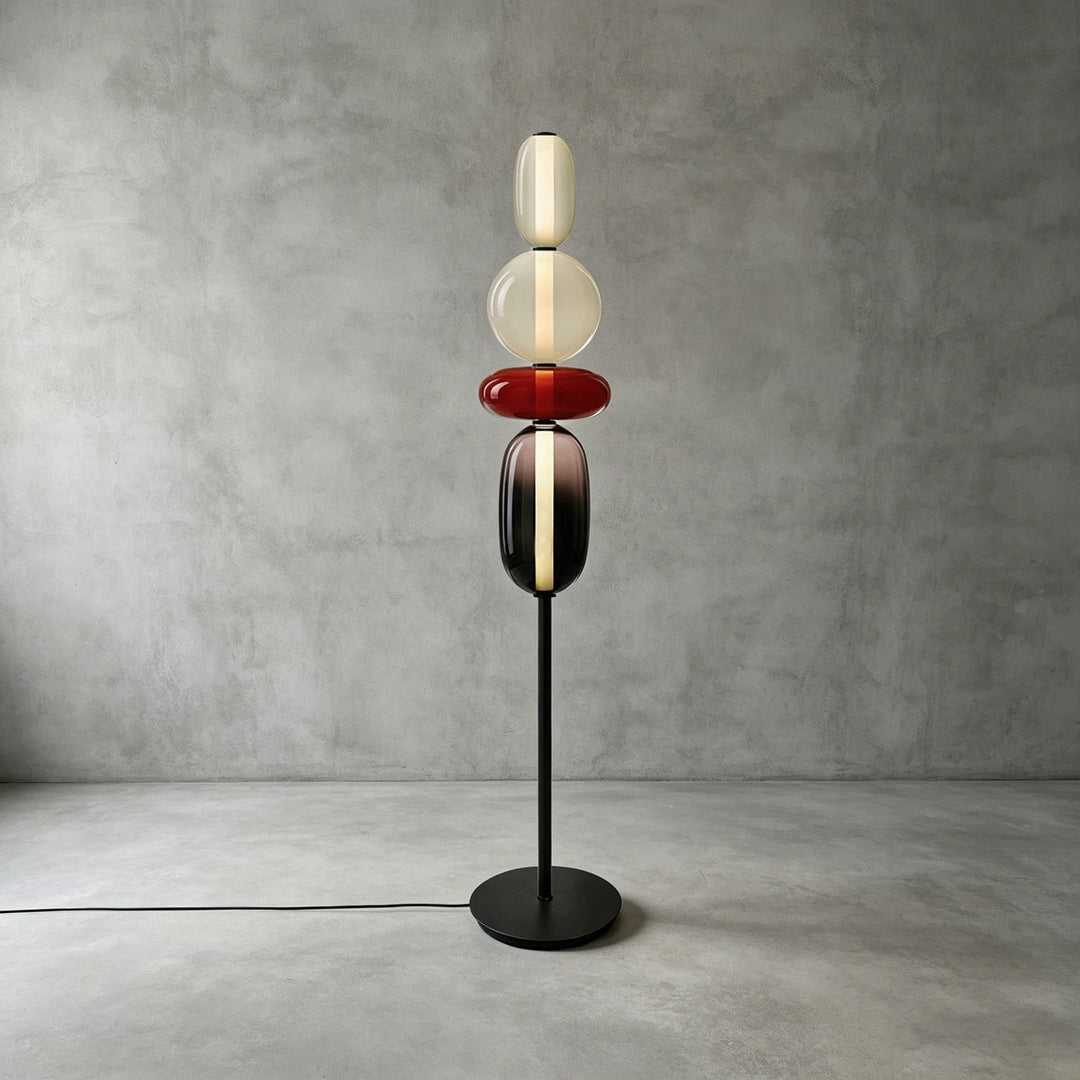 Tall Candied Model A Red glass floor lamp with a warm illuminated core against a concrete wall.