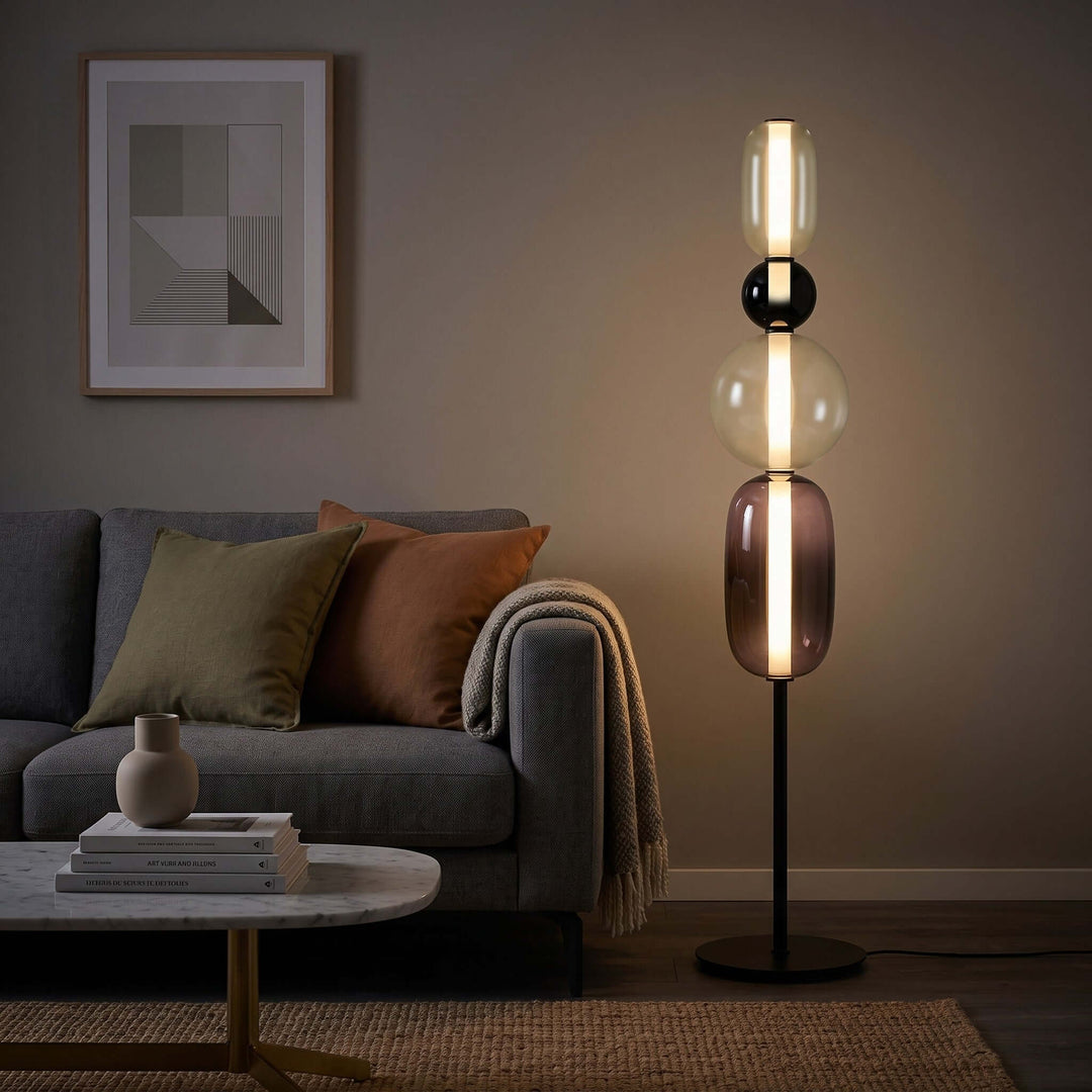 Candied Model B Black floor lamp casting warm light beside a dark sofa in an evening living room.
