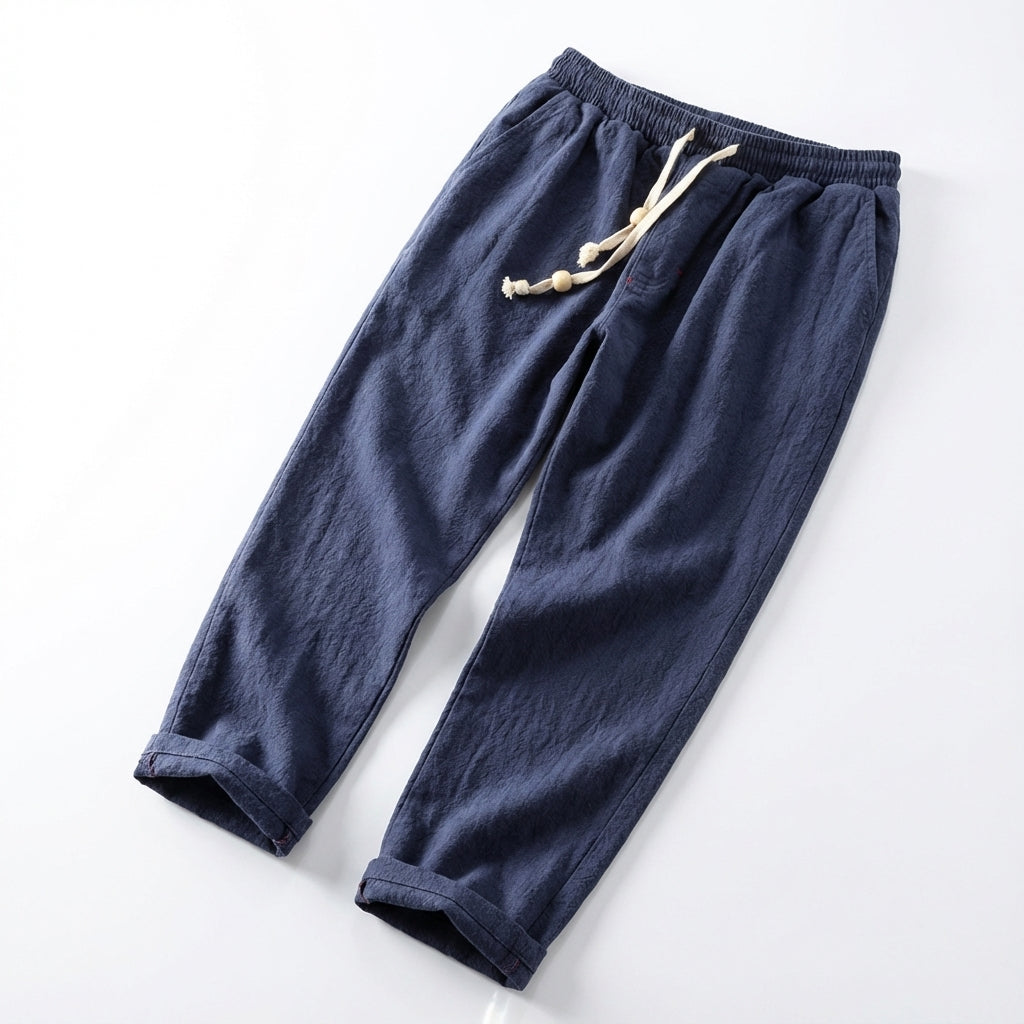 A high-angle shot of the Japanese Flow Trousers laid flat on a minimalist white studio background, illuminated with softbox lighting to highlight the intricate handcrafted stitching and natural cotton texture, shot using a Canon EOS 5D Mark IV with a 50mm 