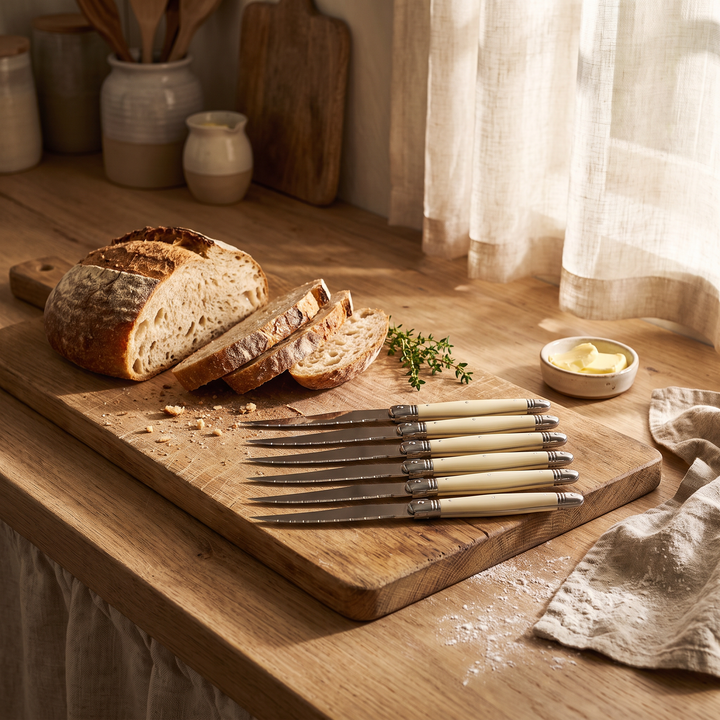Ivory Handle Stainless Silverware Set 6-piece knife set on a kitchen cutting board with bread