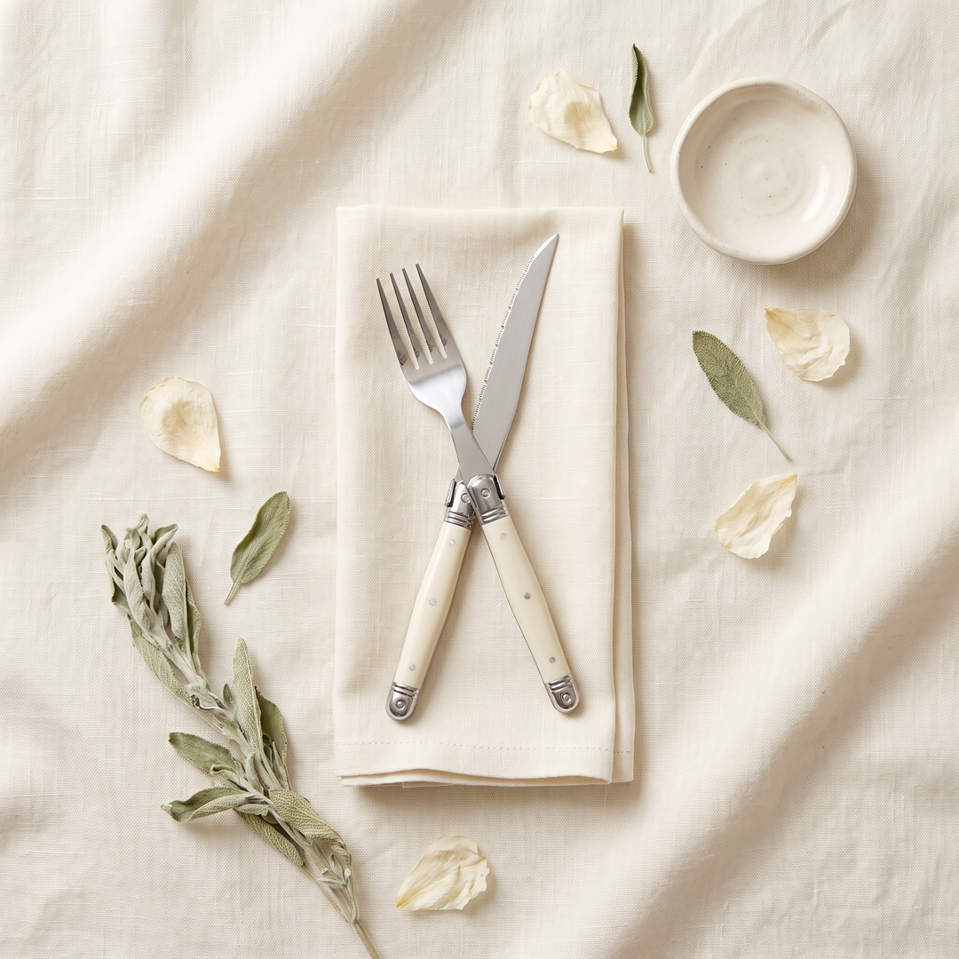 Ivory Handle Stainless Silverware Set fork and knife crossed on a linen flat lay