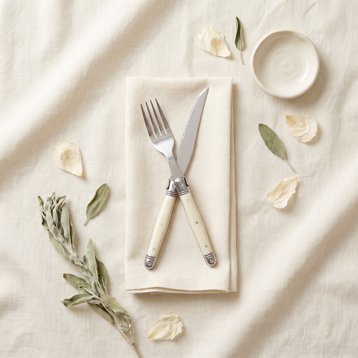 Ivory Handle Stainless Silverware Set fork and knife crossed on a linen flat lay
