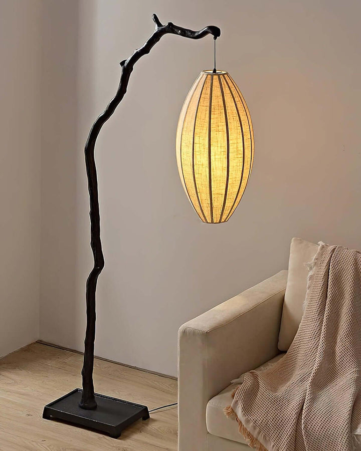 Black tree floor lamp with a glowing shade beside a cushioned armchair.