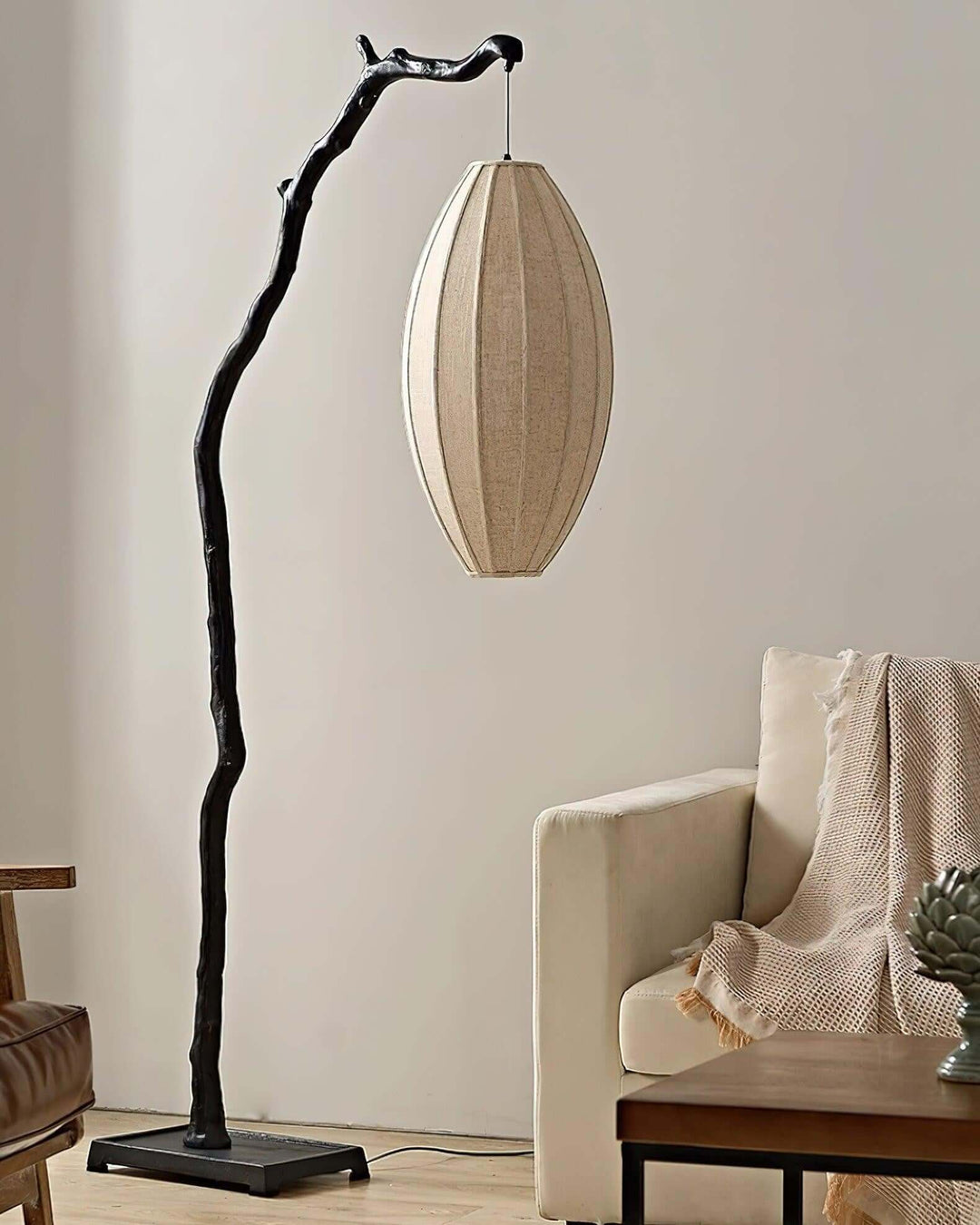 Black tree floor lamp with an unlit oval fabric shade beside an armchair.