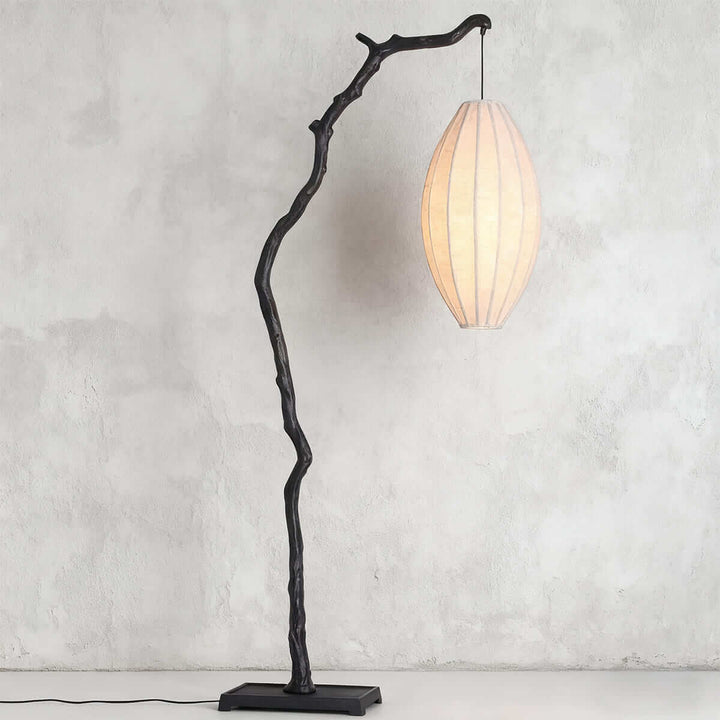 Side view of a black tree branch floor lamp with an oval fabric shade.