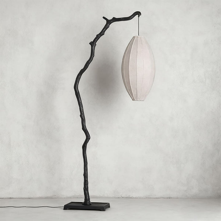 Black tree branch floor lamp with a pale unlit oval fabric shade on a gray wall.