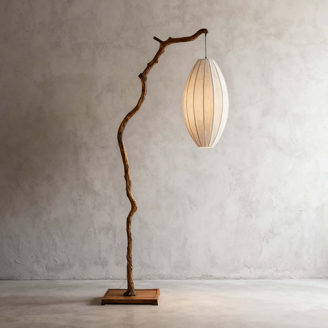 Brown tree floor lamp with an oval fabric shade shown against a gray wall.