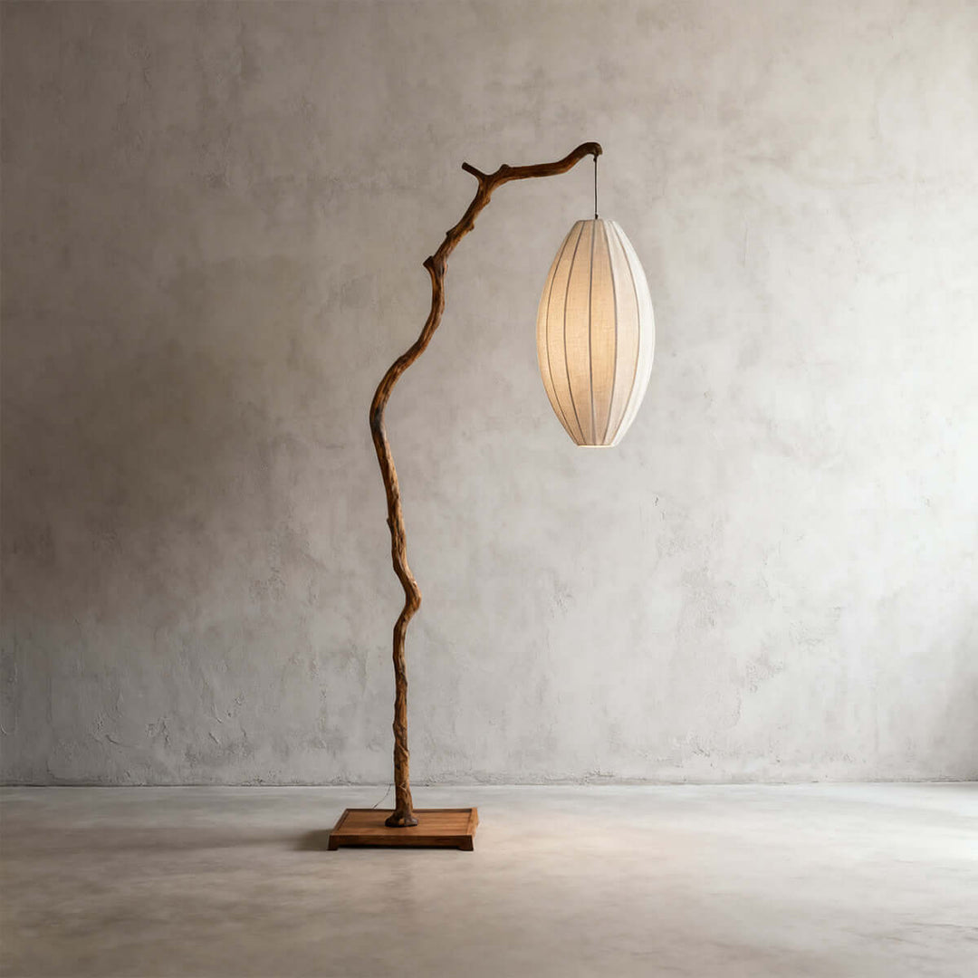 Brown tree branch floor lamp with a glowing oval fabric shade on a gray wall.
