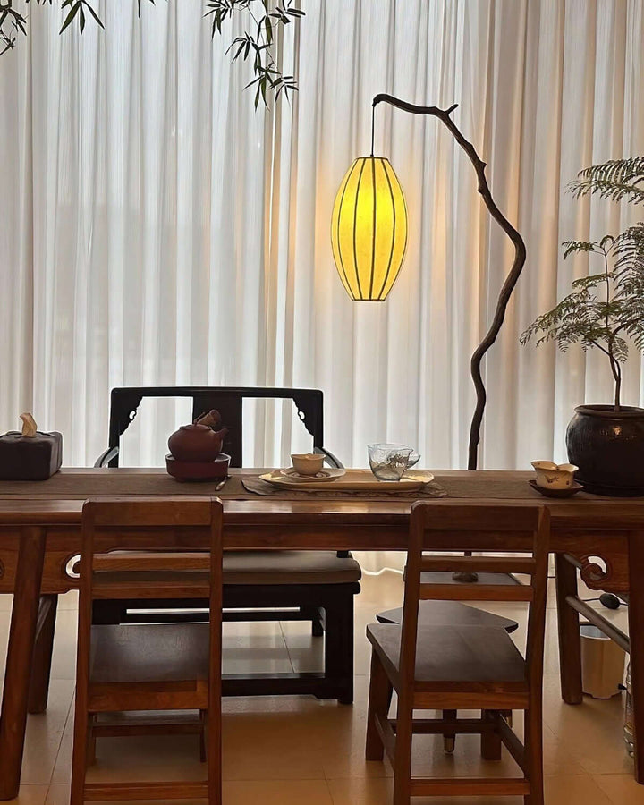 Tree floor lamp glowing beside a dining table and window curtains.