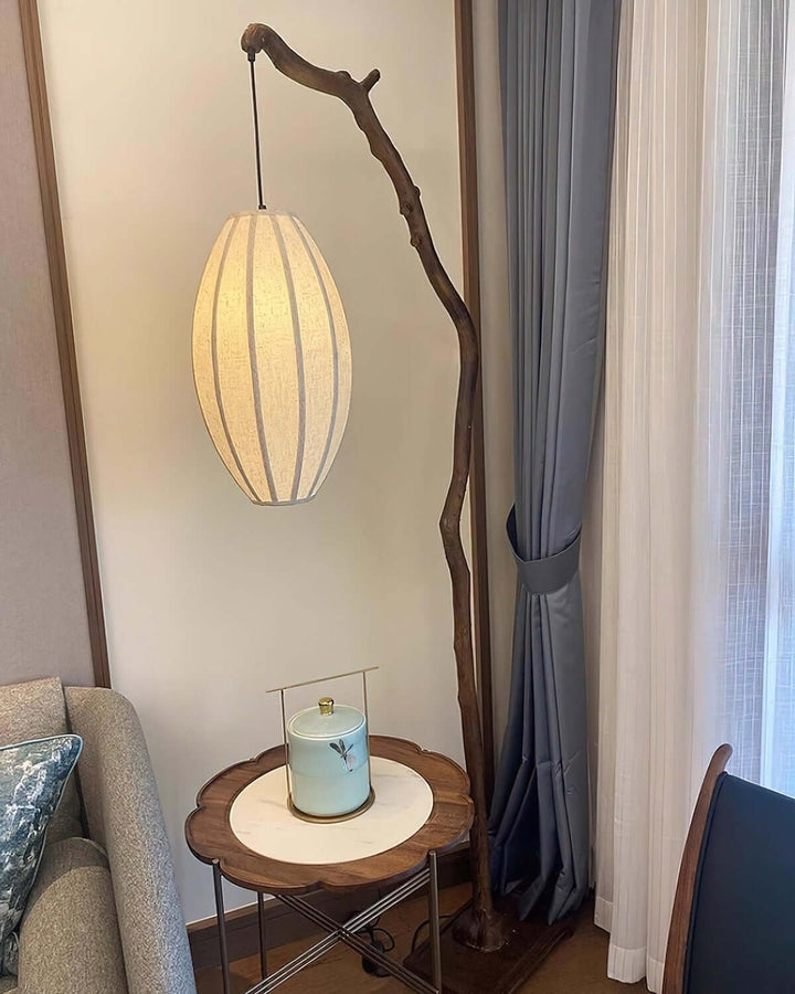 Tree floor lamp glowing beside a small round side table near curtains.