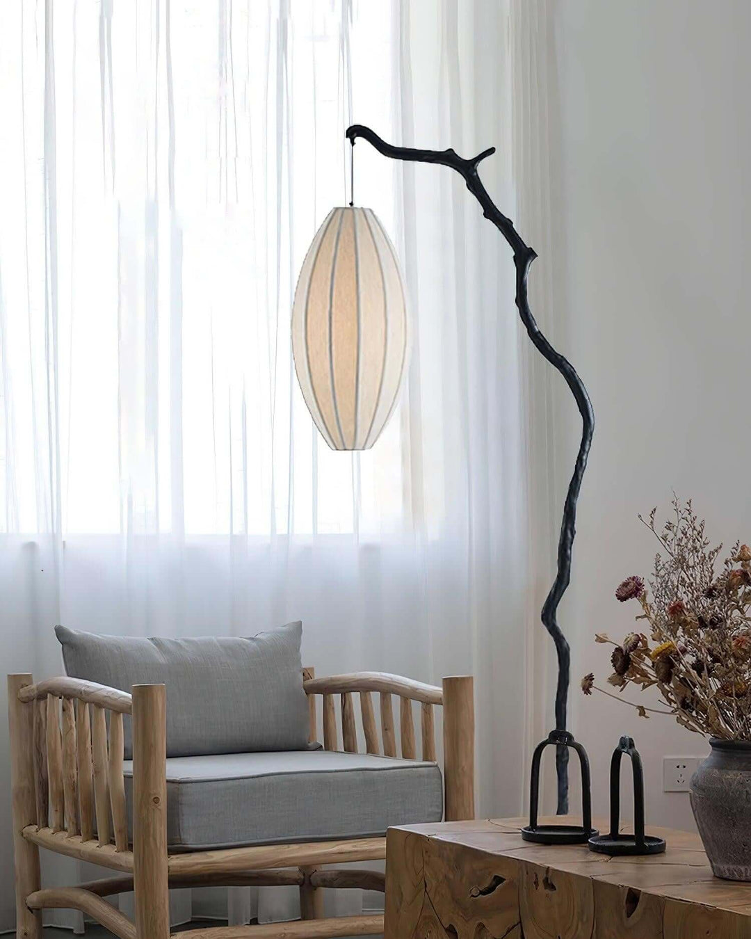 Tree floor lamp with a pale oval shade beside chairs near a bright window.
