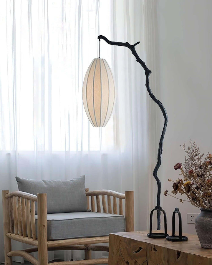 Tree floor lamp with a pale oval shade beside chairs near a bright window.